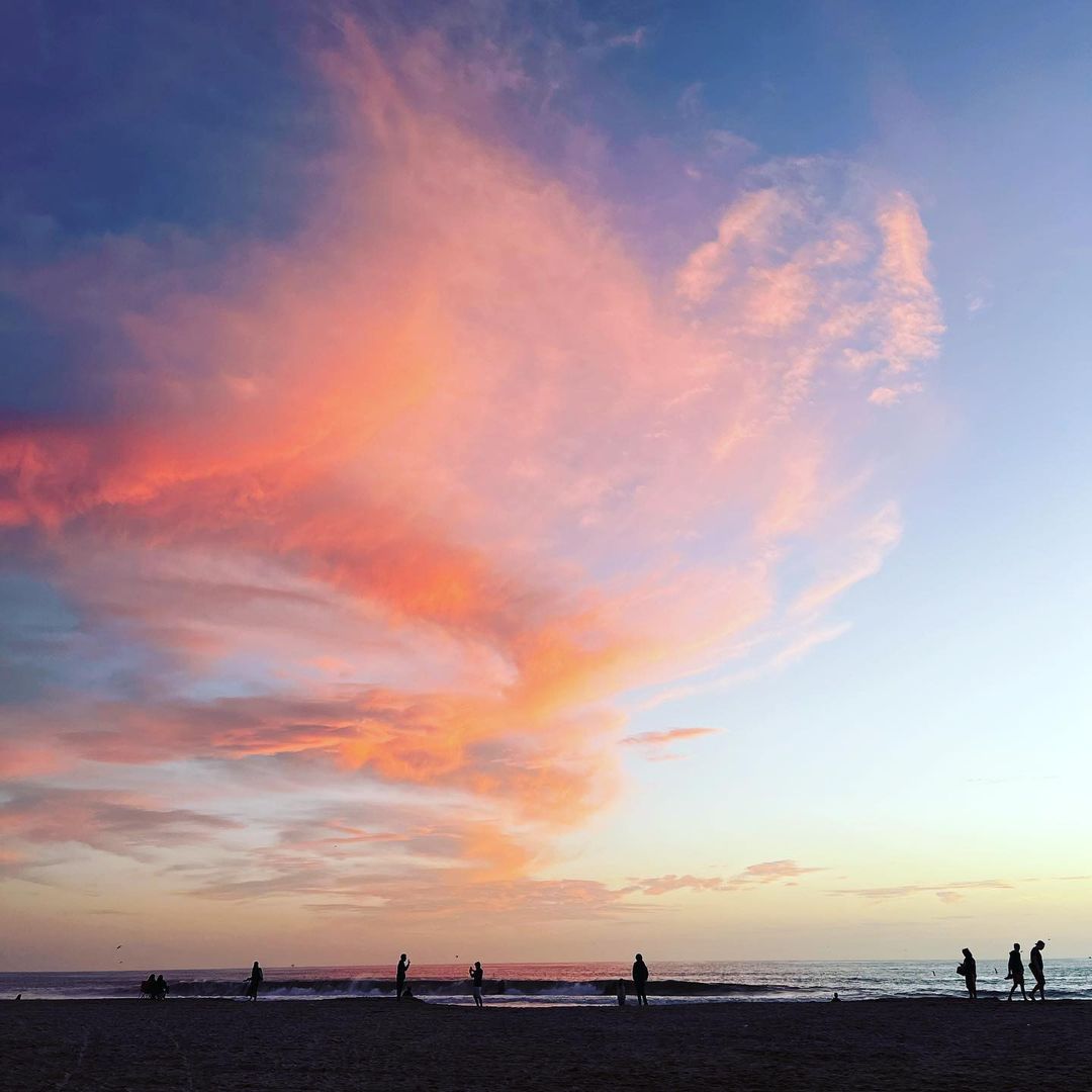 Sunset at the beach with colorful clouds in the sky and silhouettes of people walking along the shoreline in the evening.