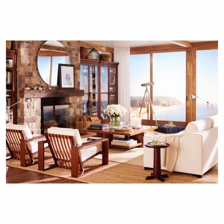 Living room interior featuring a stone fireplace, wood furniture, white sofa, and coastal view through a large window. Home interior decor.