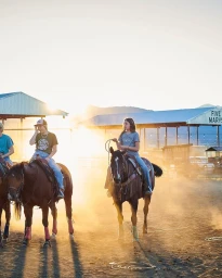 Three young riders on horseback in a dusty outdoor arena during golden hour, photographed by Mikkel Vang.