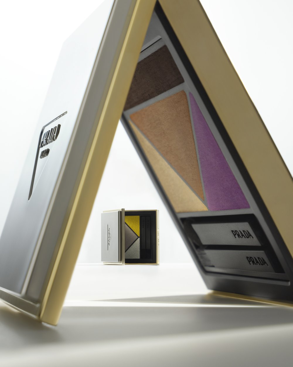 Prada makeup palette featuring brown, bronze, and purple hues, with Prada text visible on the components in a bright studio setting.