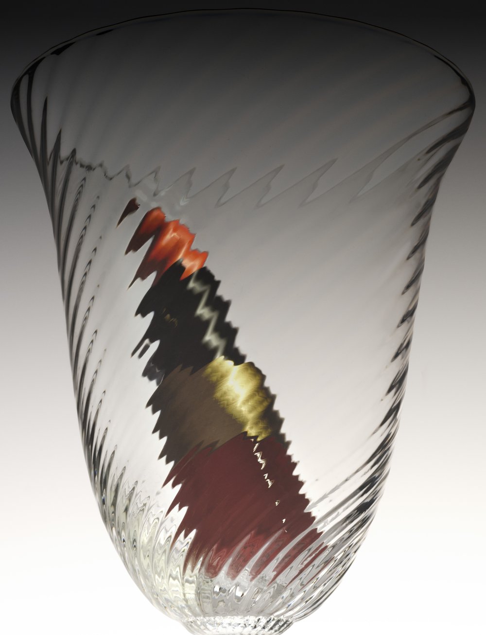 Close-up studio shot of an empty clear glass with patterned textures, displaying distorted reflections of unseen, colourful objects.