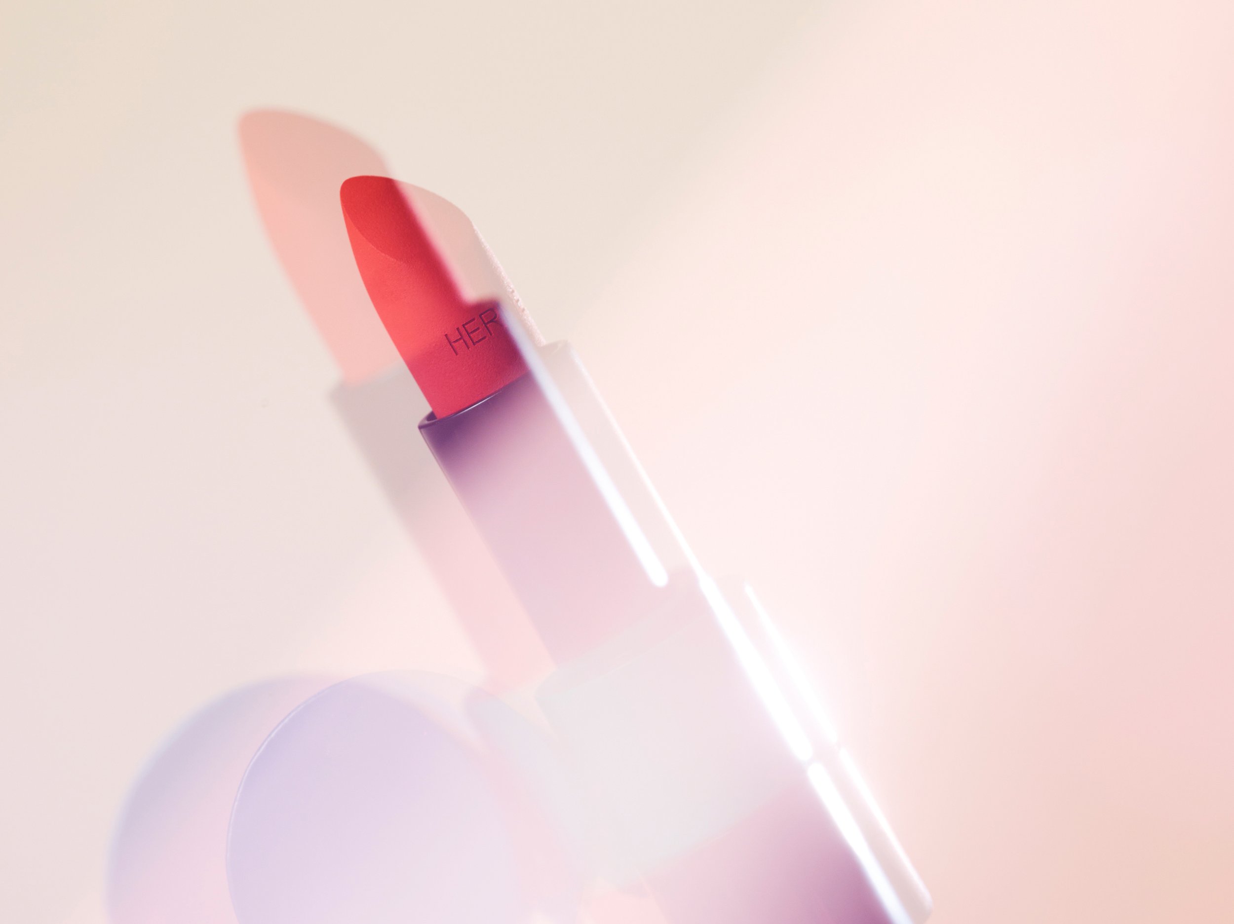 Close-up of a lipstick tube featuring a vibrant red hue against a soft, pastel-toned background creating a minimalist beauty shot.
