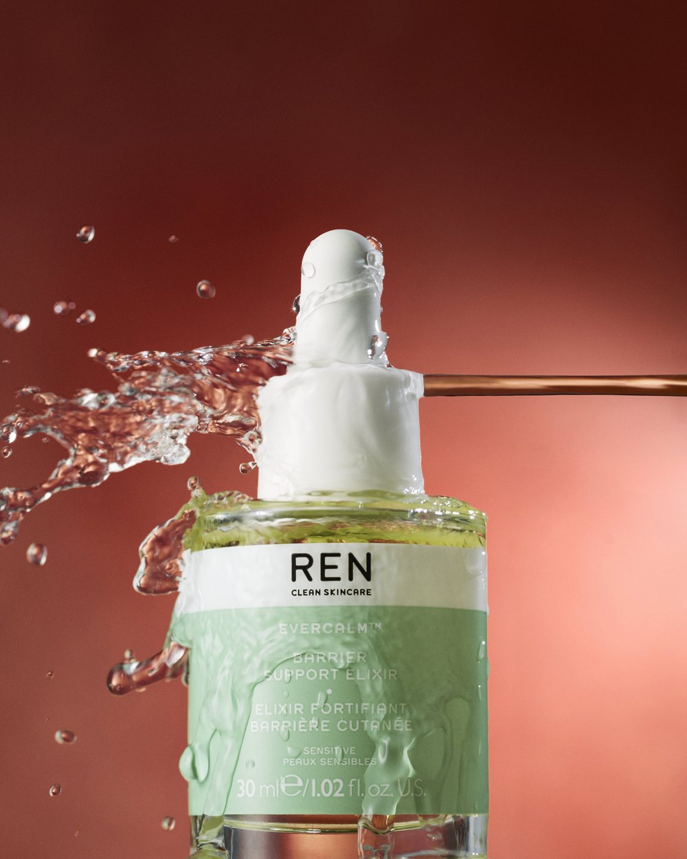 Cosmetic product photography showcasing REN Evercalm Barrier Support Elixir with water splash against a gradient red background.