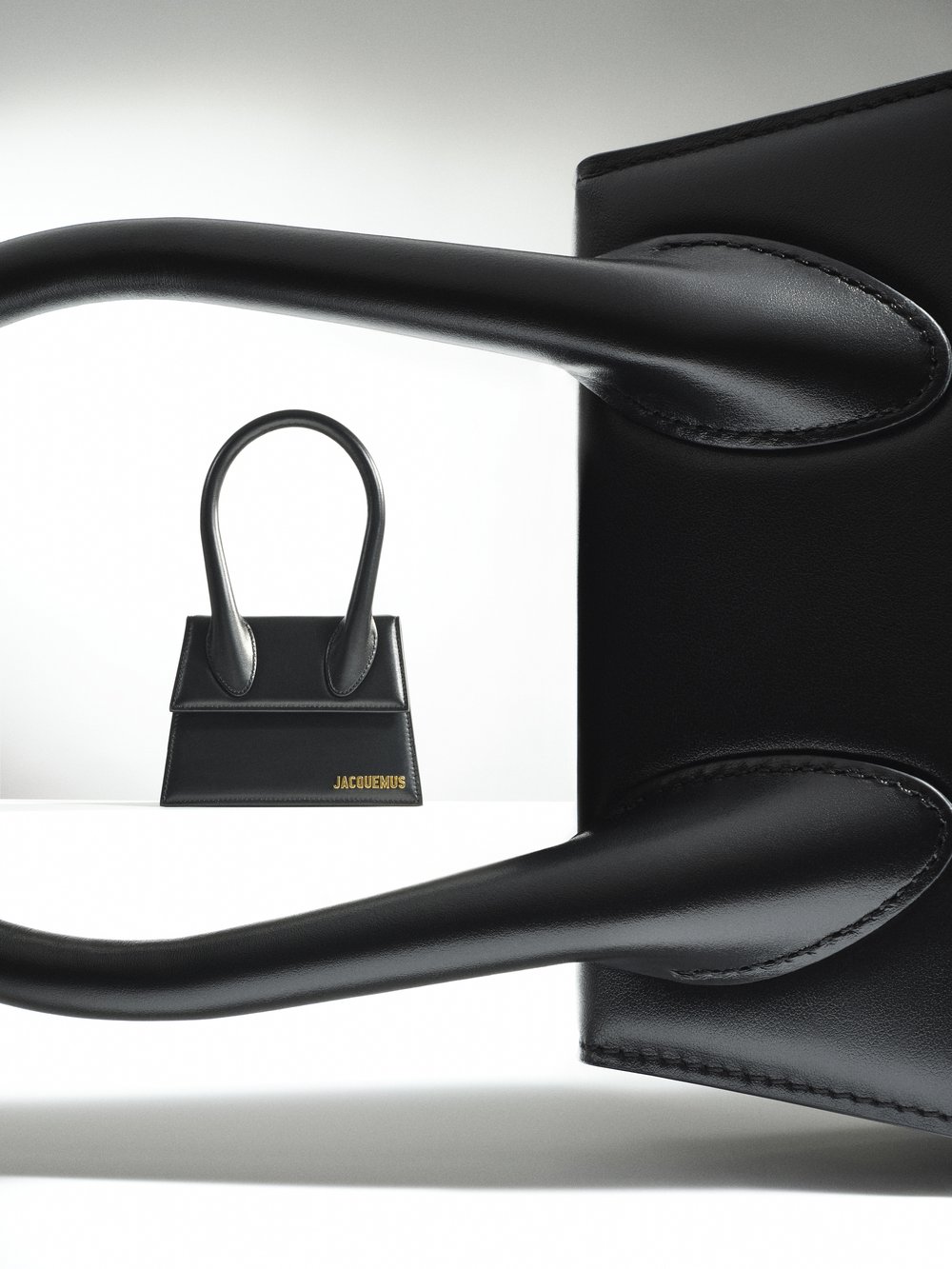 Two black leather Jacquemus bags are displayed against a white backdrop, with a smaller version in front of a larger one.