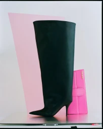 Tall black leather boot on a reflective surface with a pink panel and pink handbag set design by Carrie Louise
