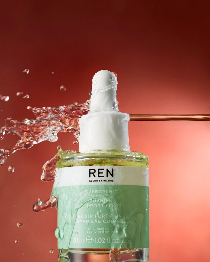 REN skincare bottle splashing with water droplets against a warm reddish background