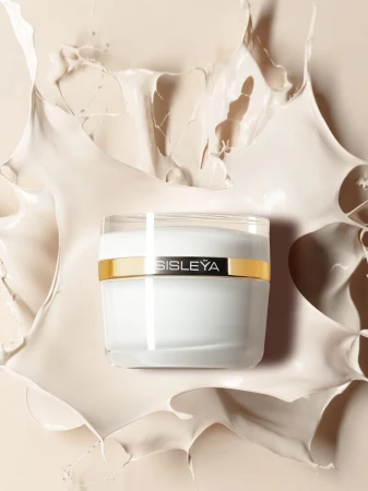 Sisley cream jar surrounded by splashing beige liquid against a beige background in a product shot.