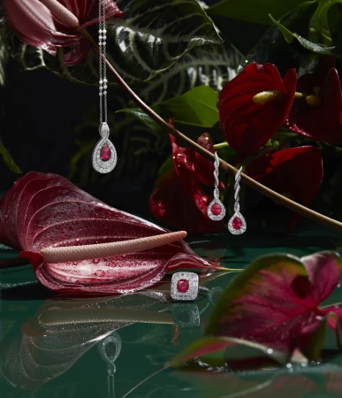 Elegant jewellery set featuring necklace, earrings, and ring with rubies and diamonds, displayed among vibrant red Anthurium flowers.