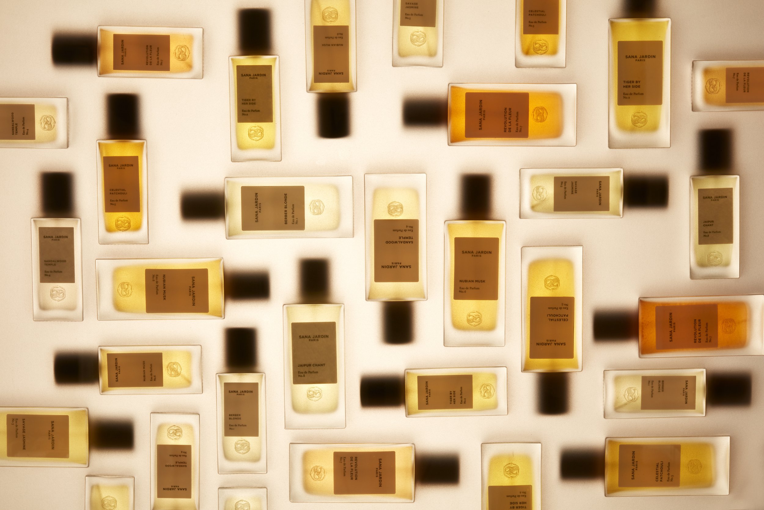 Overhead shot of an array of Sara Jardin perfume bottles on a pale background, creating a visually appealing pattern with shadows.