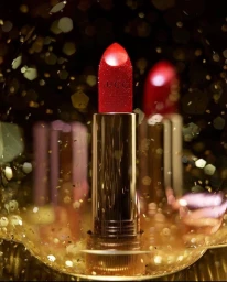 Red Gucci lipstick in a metallic gold tube surrounded by sparkling bokeh and gold confetti against a dark background.
