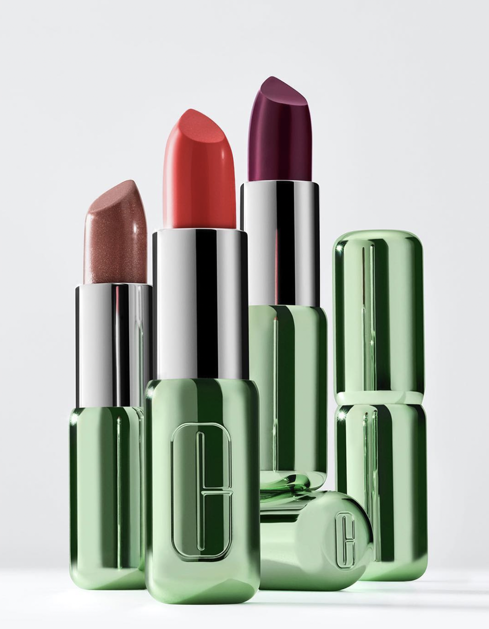 Close-up shot of lipstick tubes in varying shades of nude, coral, and plum, with metallic green and silver packaging on a white background.