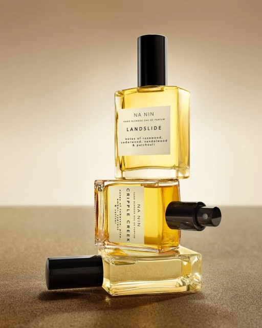 Stacked clear glass perfume bottles with black caps against a gradient beige background, product photography for fragrance brand.
