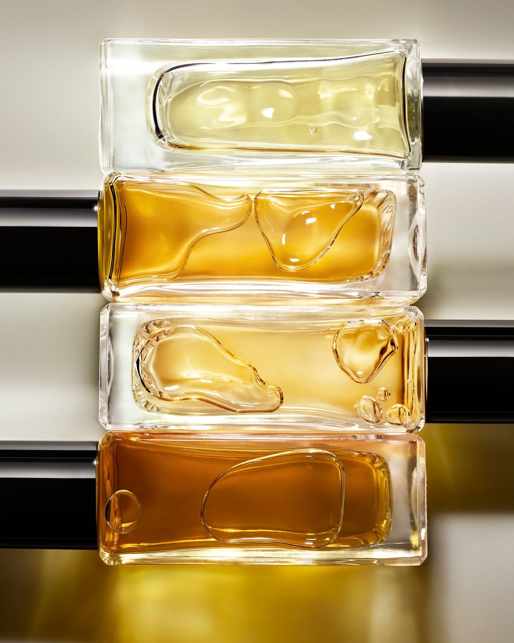 Stacked glass perfume bottles with gold liquid on neutral background. Close-up product photography for Beauty industry.