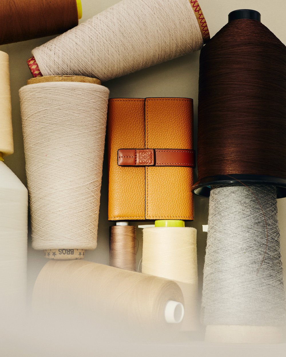 Eye-level shot showcasing spools of yarn and a leather-bound journal with a brown strap and clasp, arranged on a light surface.