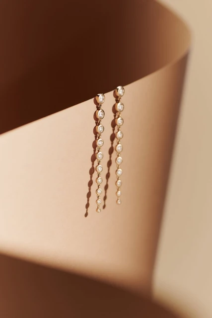 Elegant gold drop earrings with diamonds on display with dramatic lighting and soft shadows against a neutral backdrop, jewelry photography.