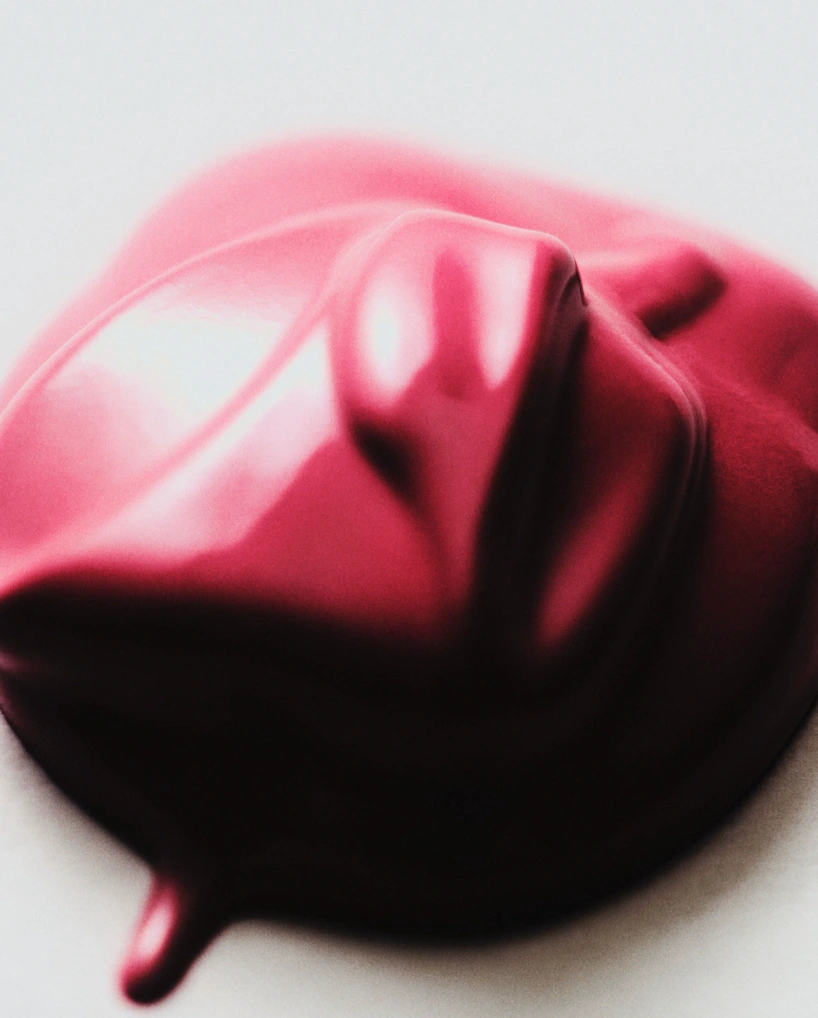 Close-up macro shot of a thick, glossy dollop of dark pink cosmetic cream on a smooth white surface.