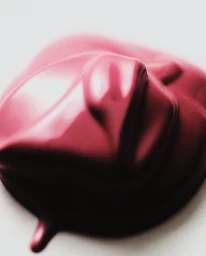 Close-up macro shot of a thick, glossy dollop of dark pink cosmetic cream on a smooth white surface.