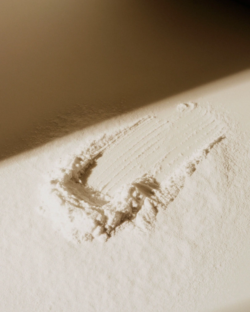 Close-up of a smooth circular cosmetic powder swatch on a warm beige surface under directional light.