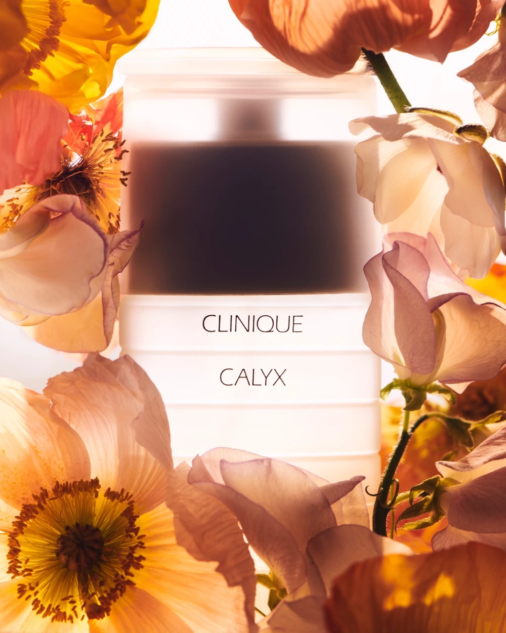 Clinique Calyx perfume bottle framed by warm backlit yellow and pink flowers set design by Laura Woolf