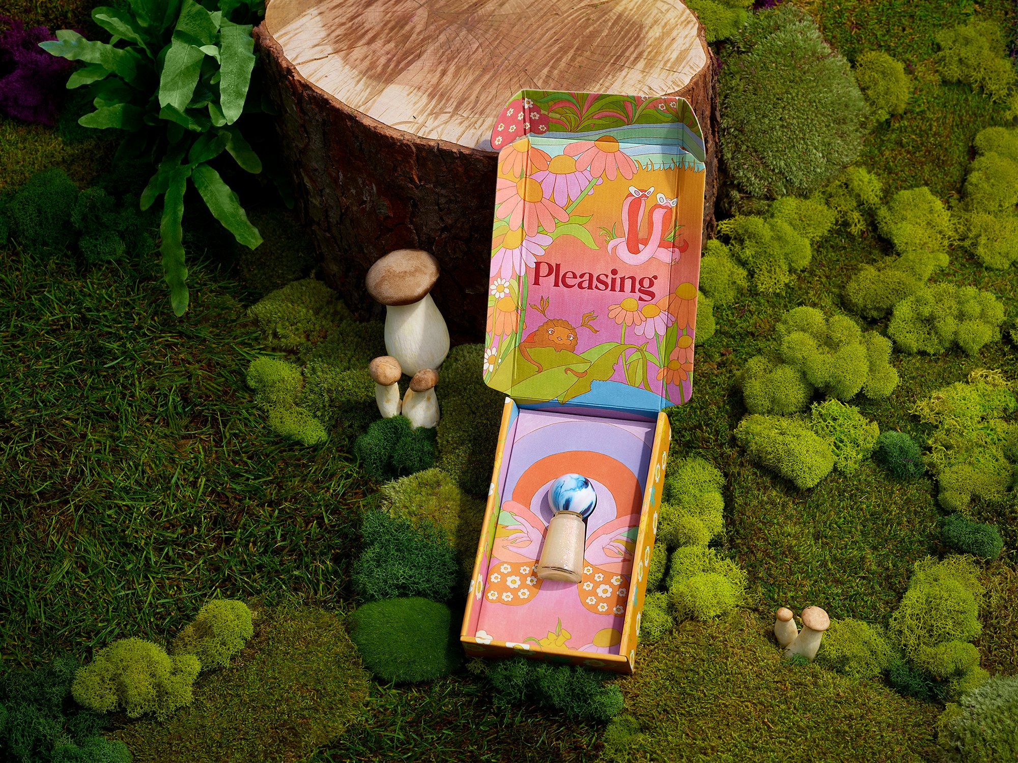 A product box from Pleasing sits open on a mossy surface, featuring a mushroom-shaped object inside and miniature mushroom figurines.