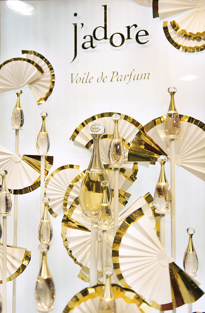 Display of J'adore Voile de Parfum bottles arranged with white and gold decorative fans in a retail setting.