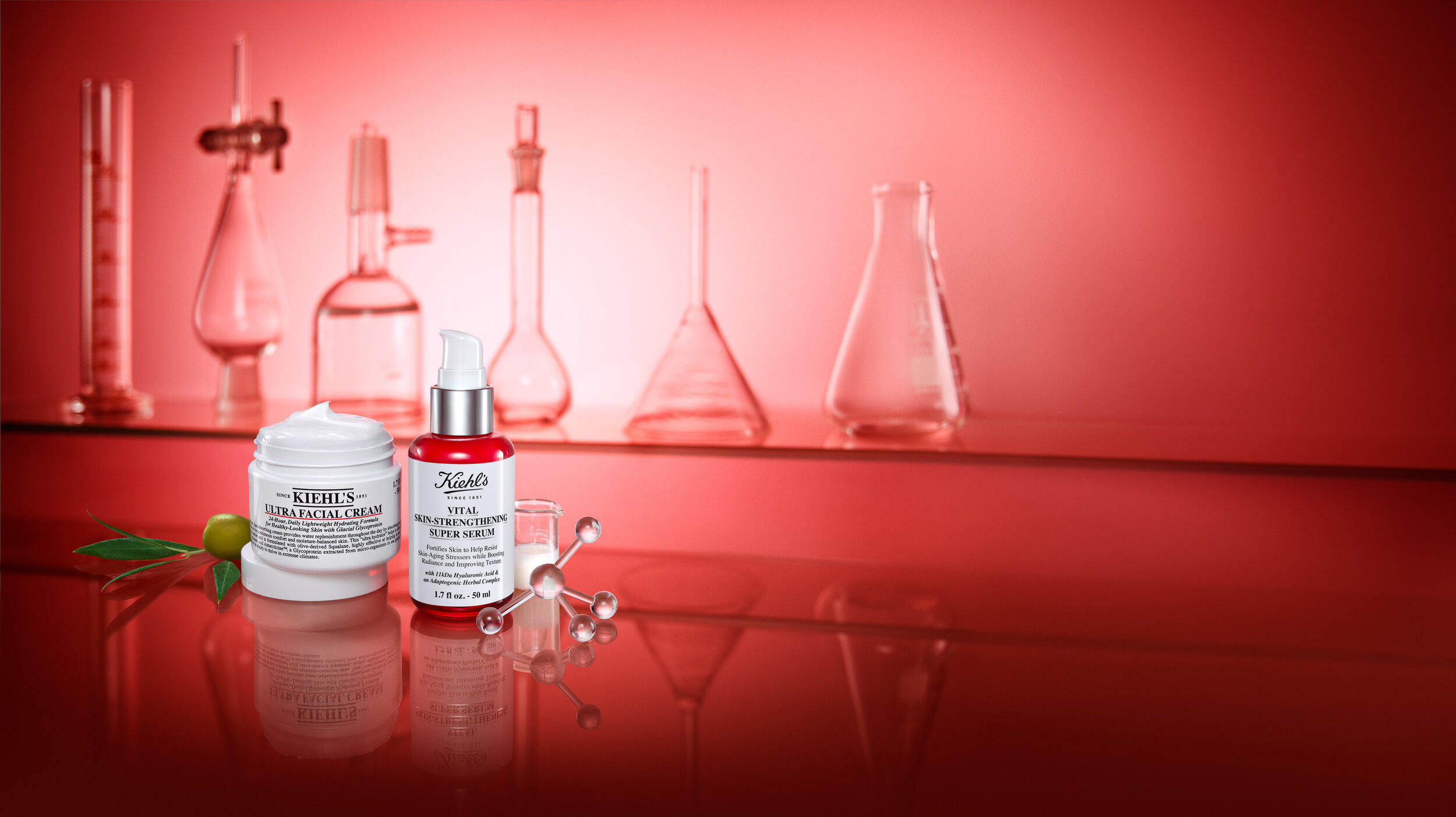 Kiehl's skincare products including cream and serum displayed with laboratory glassware on a reflective red surface, beauty photography.