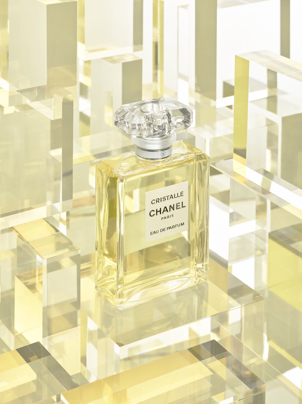Elegant still life of Chanel Cristalle Eau de Parfum showcasing its faceted bottle, transparent cap, and golden hue, set on clear geometric platforms.