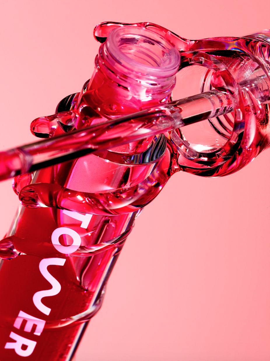 Clear plastic beauty product container filled with pink liquid, angled, on light pink background in a beauty or cosmetics still life shot.