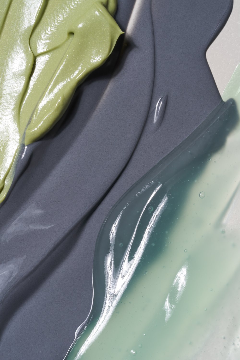 Close-up of light green, gray, and blue cosmetic product smears creates a textured pattern, suitable for beauty or skincare promotions.