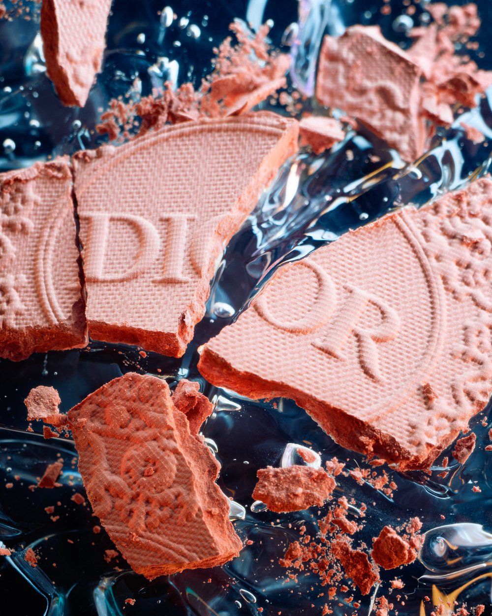 Close-up of broken DIOR eyeshadow palette with peach tones, detailed texture, and water-like gel reflections on a translucent surface.