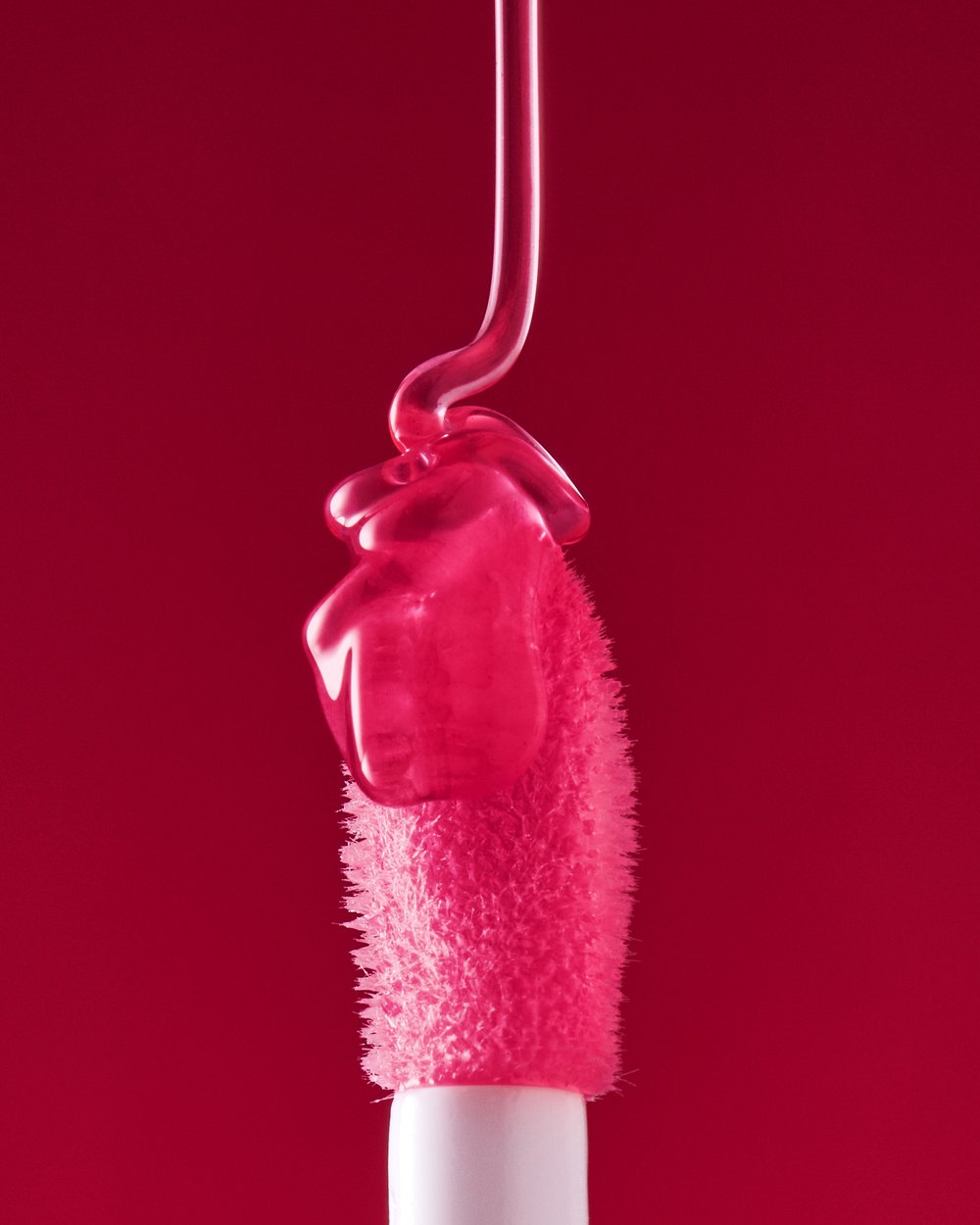 Close-up of lip gloss wand with pink liquid on red background. Beauty product, cosmetic applicator, makeup.