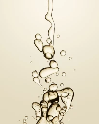 Clear liquid droplets and stream pouring down against a neutral beige background with soft lighting.