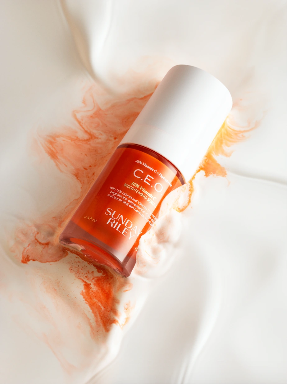 Serum bottle resting on white draped fabric with orange pigment spreading around it