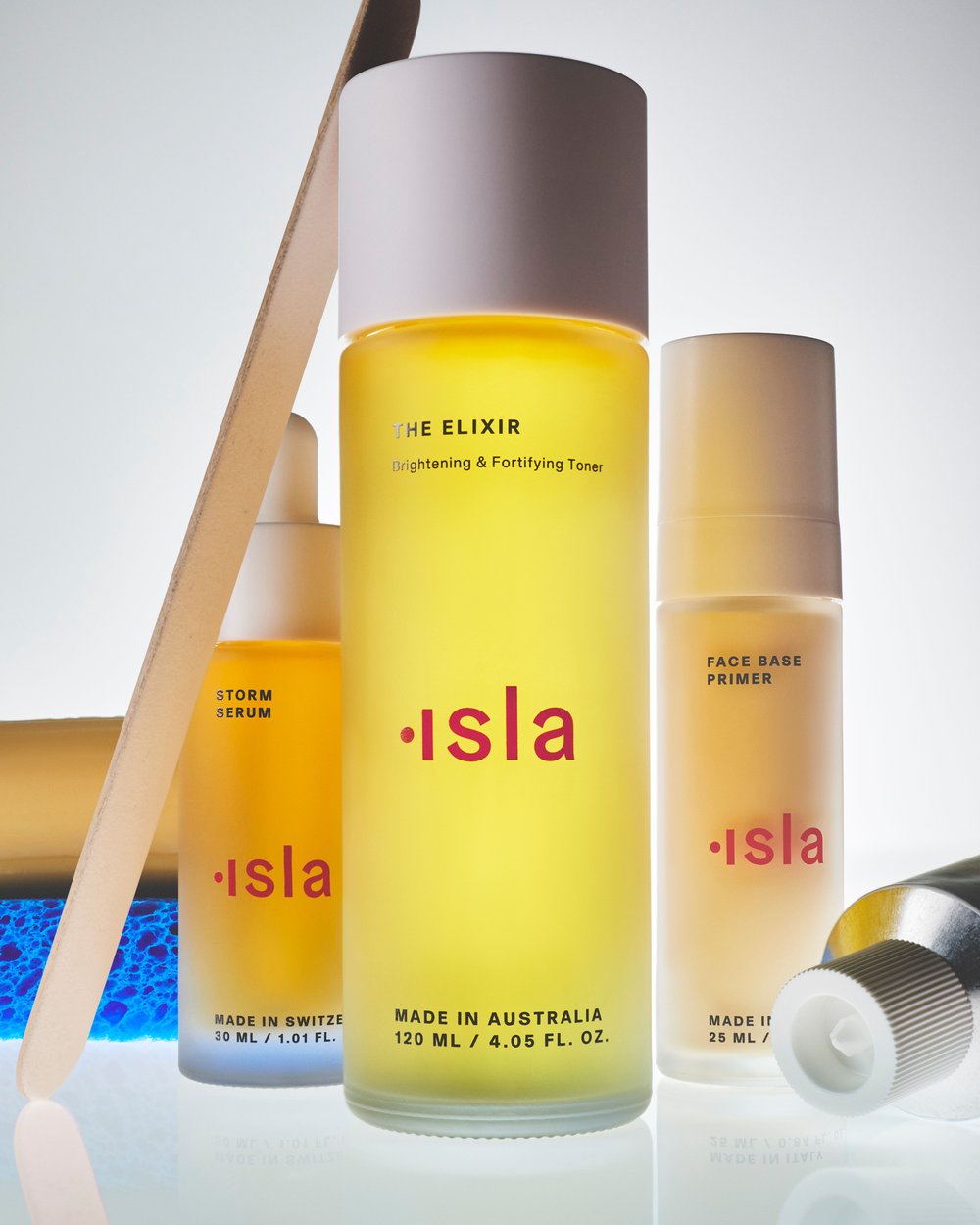 Cosmetic product bottles with labels featuring the brand name 'isla' in shades of yellow and red against a bright background.