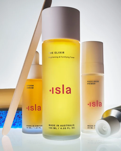 Cosmetic product bottles with labels featuring the brand name 'isla' in shades of yellow and red against a bright background.