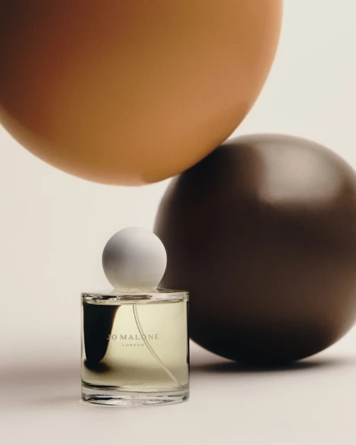 Studio shot of a Jo Malone London perfume bottle against a backdrop featuring tan and brown spherical objects, clean presentation.