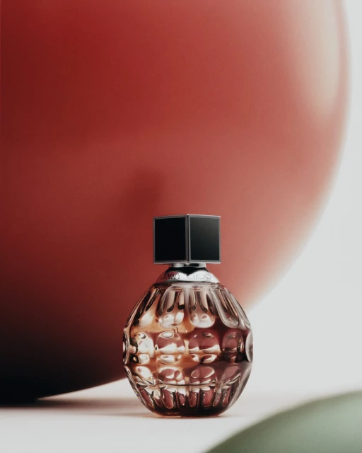 Close-up of a textured perfume bottle with a black cap, set against a red background, evoking luxury and sophistication in beauty product photography.