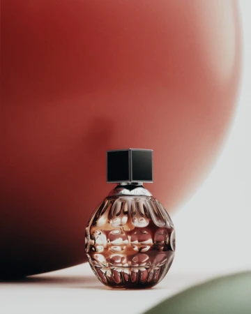Close-up of a textured perfume bottle with a black cap, set against a red background, evoking luxury and sophistication in beauty product photography.