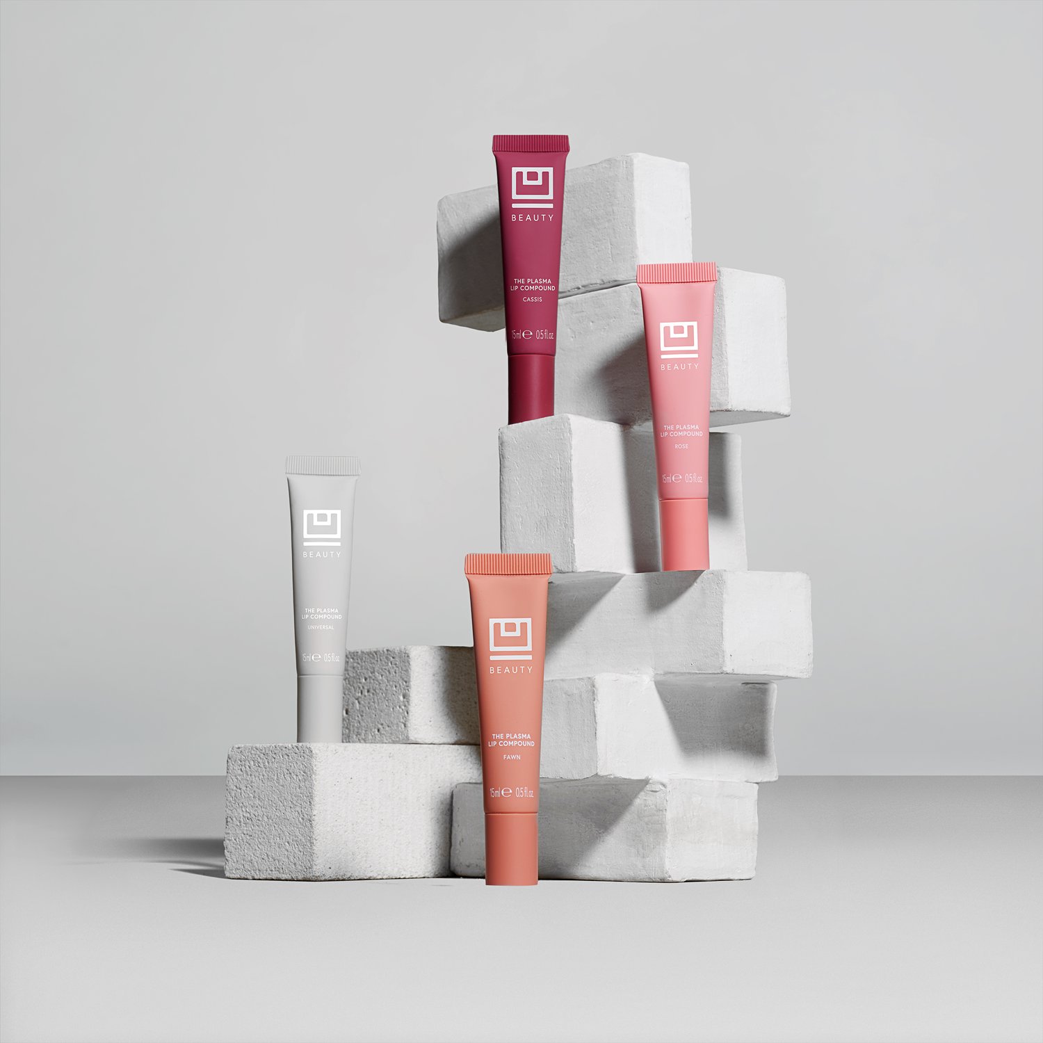 Arrangement of colorful lip products on a white geometric block display against a neutral gray studio background. Beauty product flat lay.