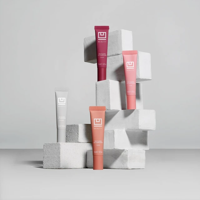 Arrangement of colorful lip products on a white geometric block display against a neutral gray studio background. Beauty product flat lay.