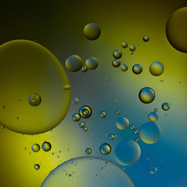 Abstract close-up shot of oil droplets in water creating colorful spheres in shades of yellow, blue, and gray with a blurred background.