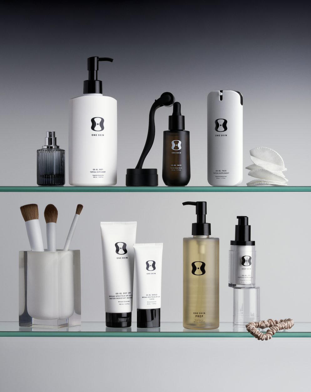Still life of skincare products on glass shelves, featuring a variety of bottles, tubes, and makeup brushes against a gradient gray background.