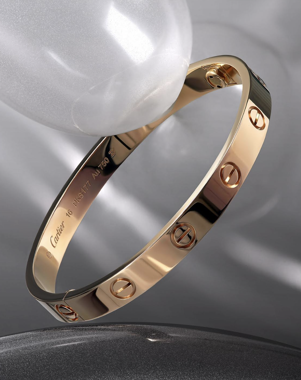 Close-up studio shot of a gold Cartier Love bracelet featuring the brand's signature screw motif, resting on a gray surface.