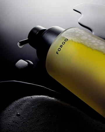 Close-up of a yellow liquid soap bottle with a black pump dispenser on a dark background with soap bubbles and liquid.