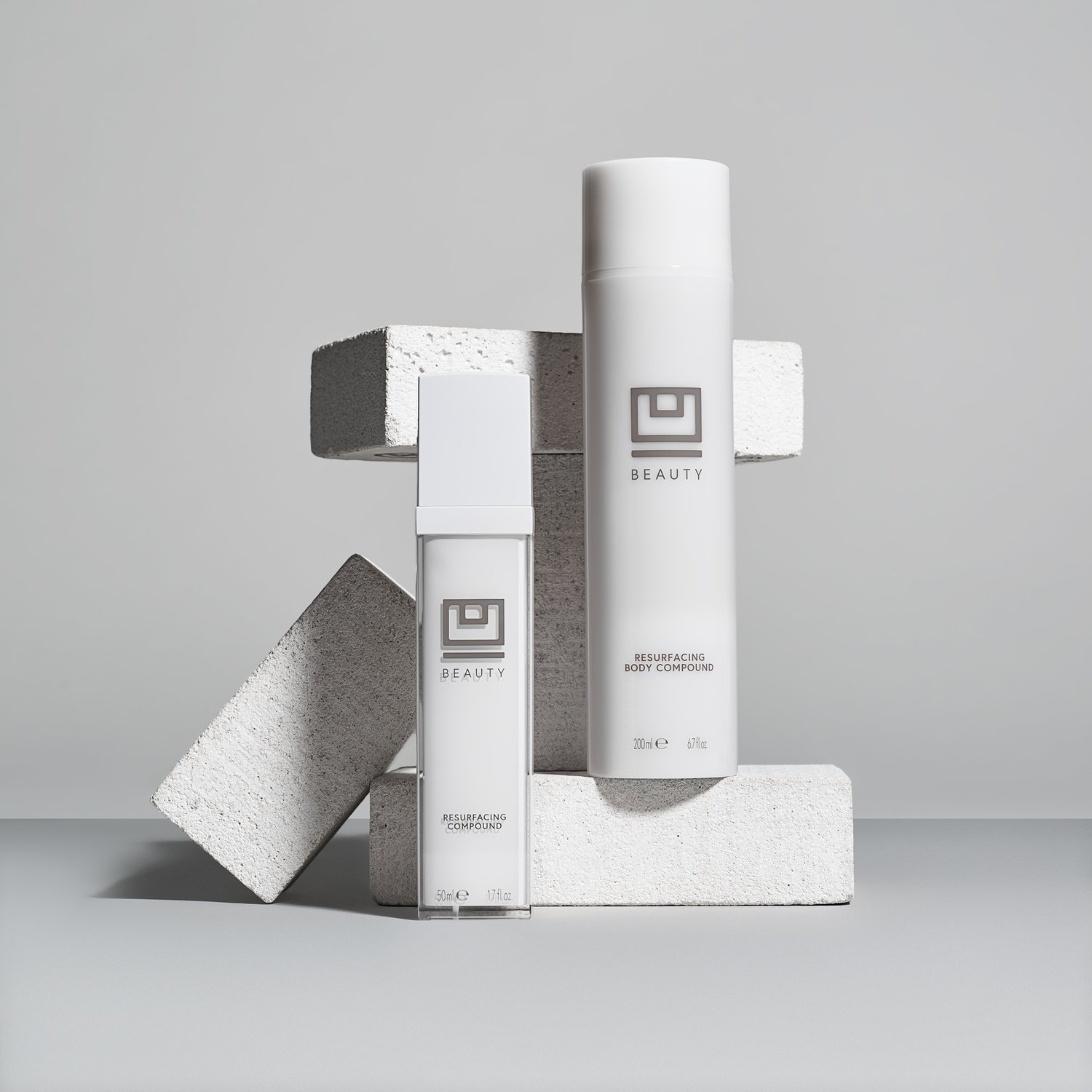 Two white cosmetic containers sit on geometric blocks against a light gray background, showcasing minimalist beauty product presentation.