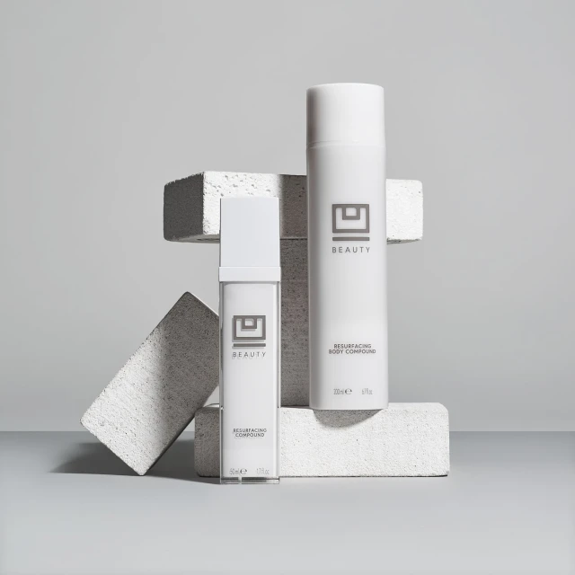 Two white cosmetic containers sit on geometric blocks against a light gray background, showcasing minimalist beauty product presentation.