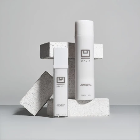 Two white cosmetic containers sit on geometric blocks against a light gray background, showcasing minimalist beauty product presentation.