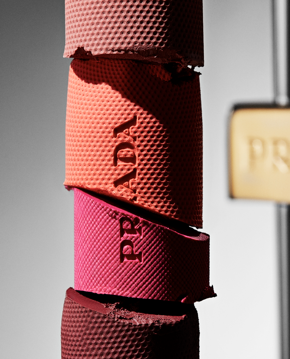 Close-up studio shot of stacked Prada blush compacts in red, pink, and coral hues, creating a textured makeup and beauty product still life.