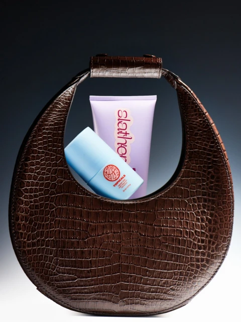 Studio shot of a brown handbag with an alligator skin texture, framing a blue and purple cosmetic container against a dark gray background.