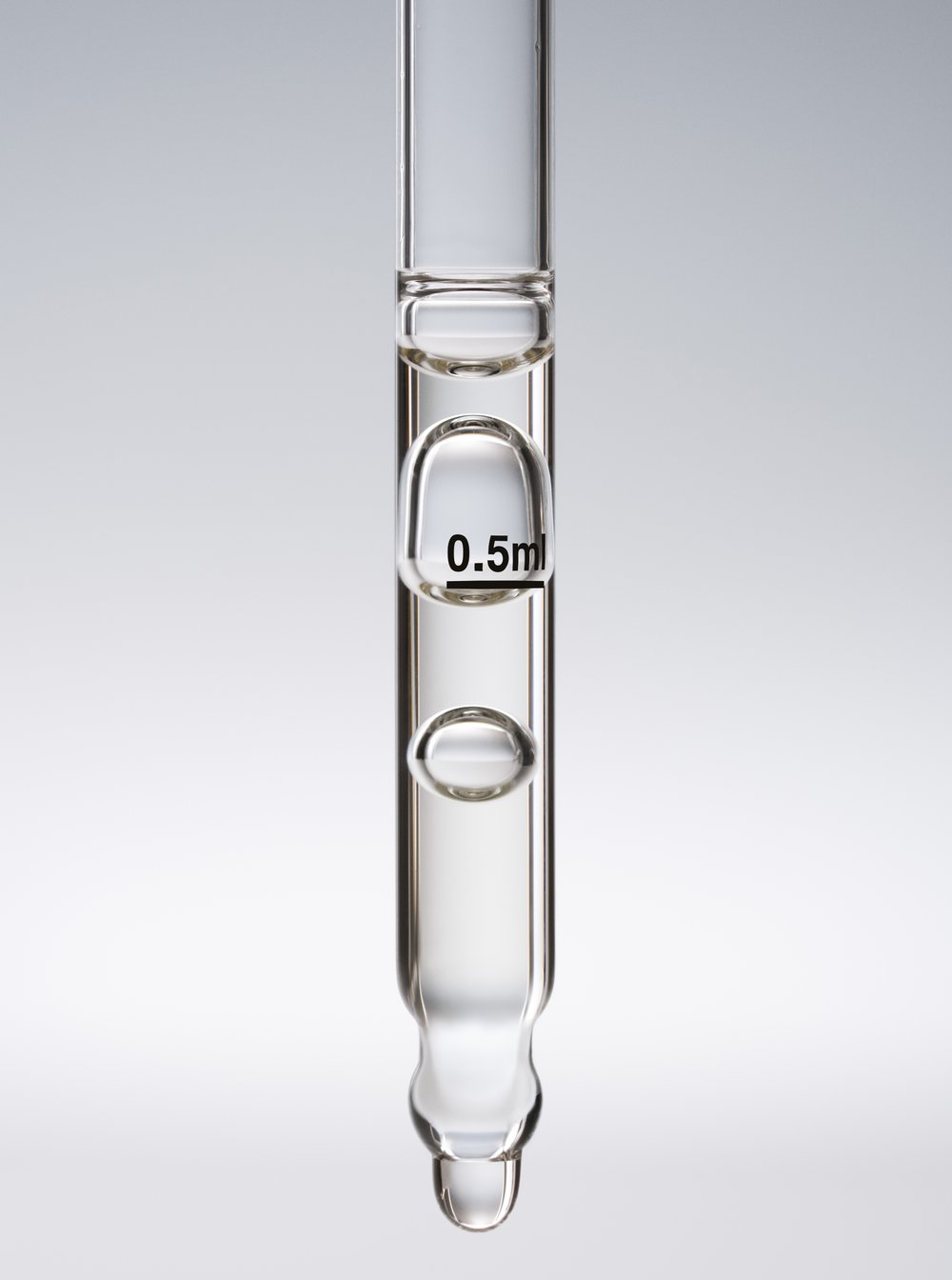 Close-up studio shot of clear glass pipette filled with liquid against a gradient gray background, displaying a liquid droplet.